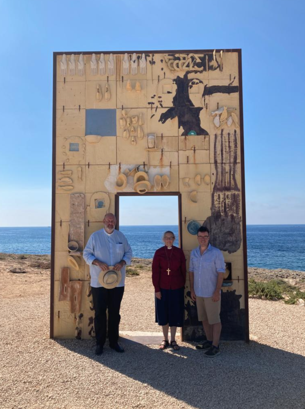 Three people standing in front of a sculpture at the beach.