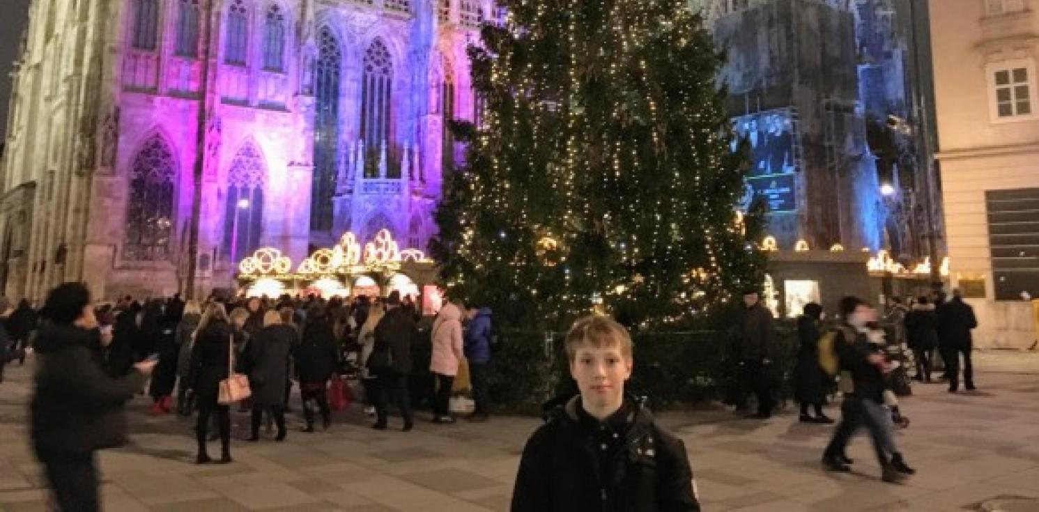 boy standing next to Christmas tress
