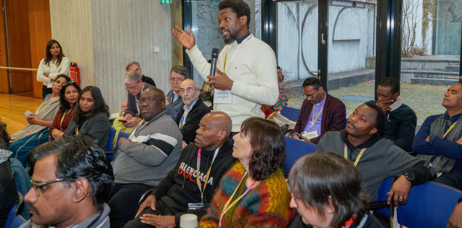 A man stands up to speak amidst others at a conference