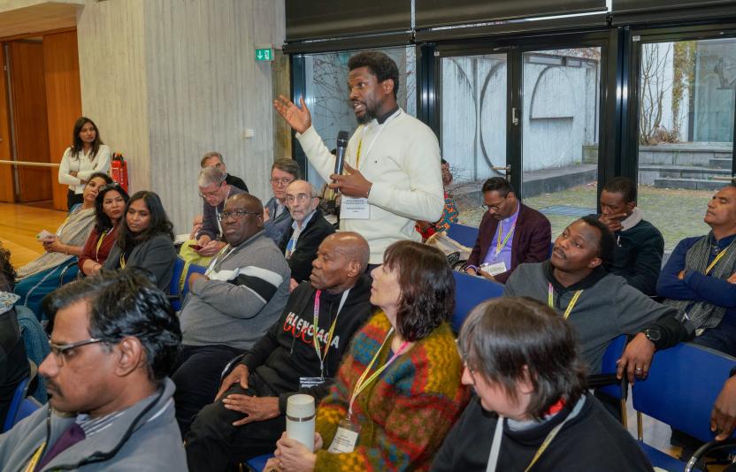 A man stands up to speak amidst others at a conference